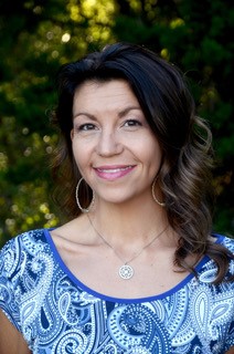 Hispanic woman with long brown hair, blue shirt with hoop earrings and necklace