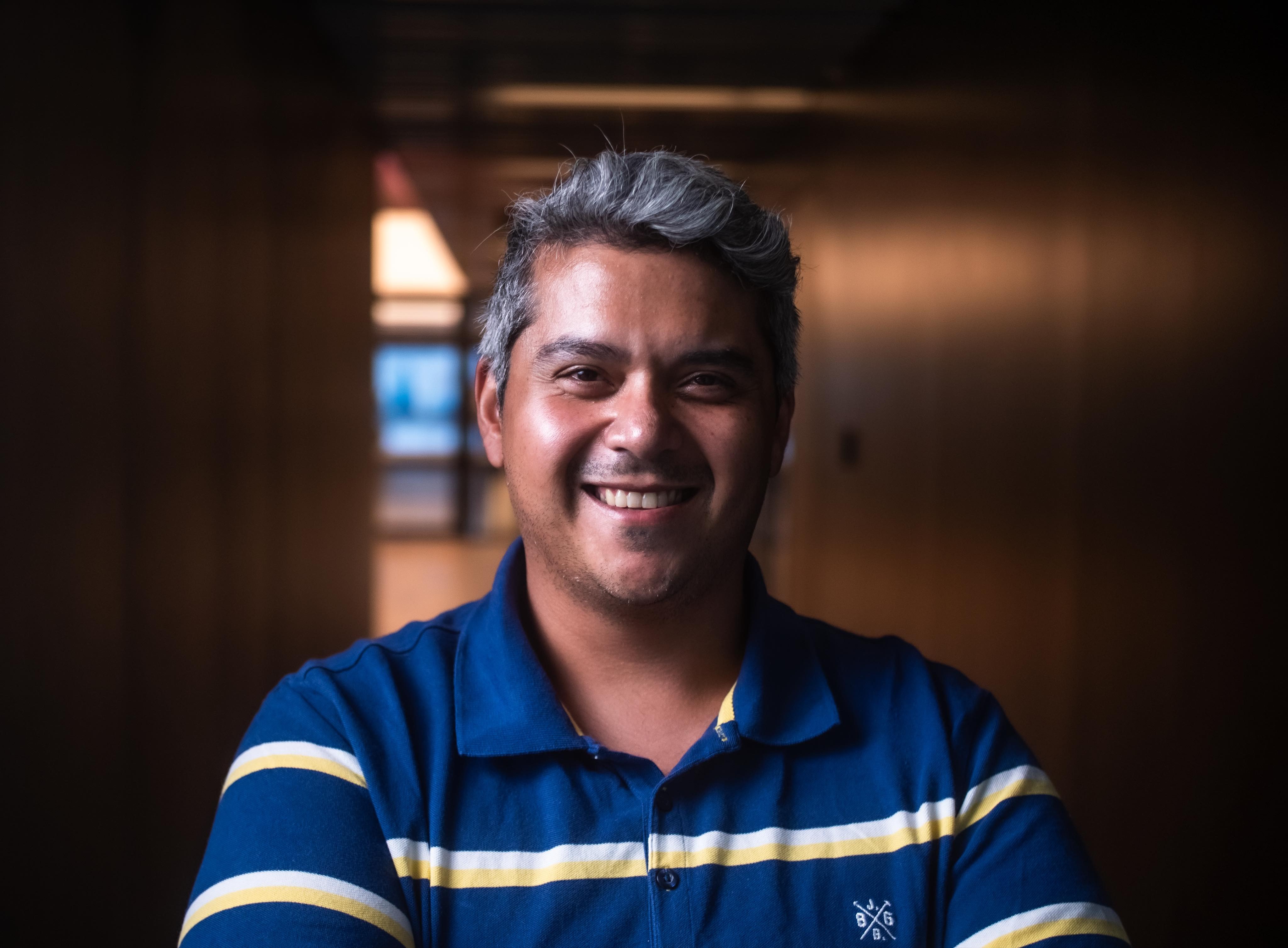 dark skin man with graying short hair in blue and white striped collared shirt