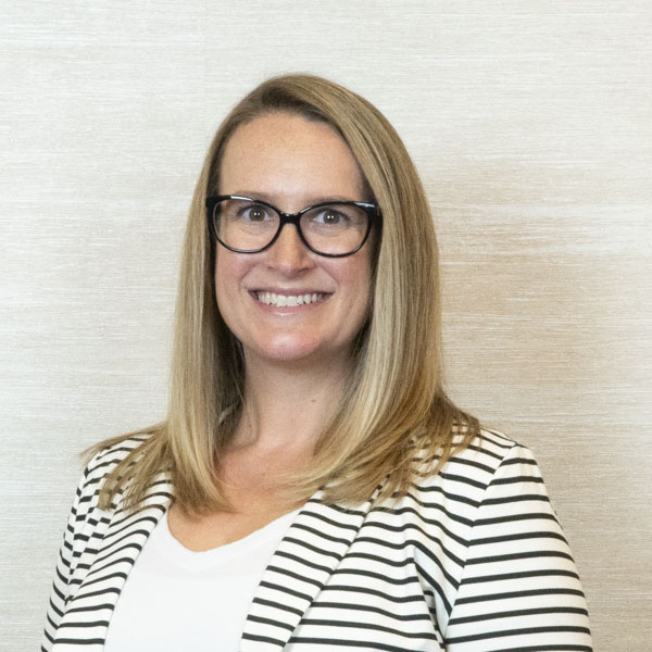 white woman with shoulder-length blonde hair, black and white striped jacket, white shirt, and glasses